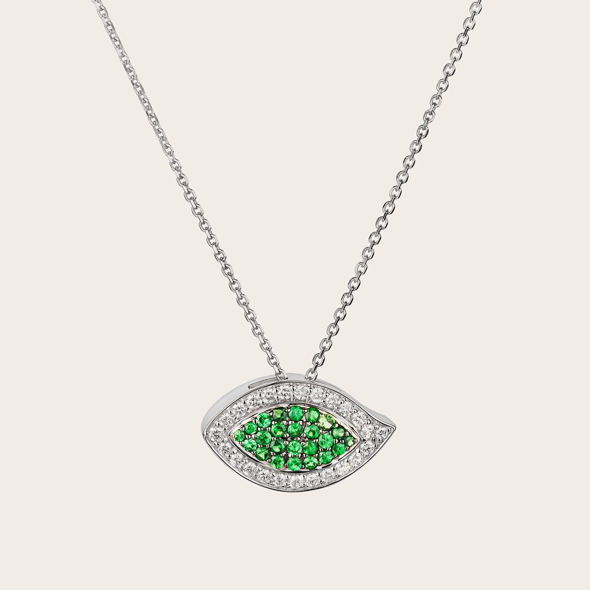 This image shows a close up view of the Evil Eye Tsavorite and Diamond Pendant. The pendant is made of 18kt white gold and features approximately 0.34cts of sparkling white diamonds and 0.47cts of vibrant tsavorite stones. The evil eye design is a classic symbol of protection, and the combination of the tsavorite and diamonds creates a truly eye-catching look. The details of the pendant are beautifully crafted and showcase the quality of the materials.