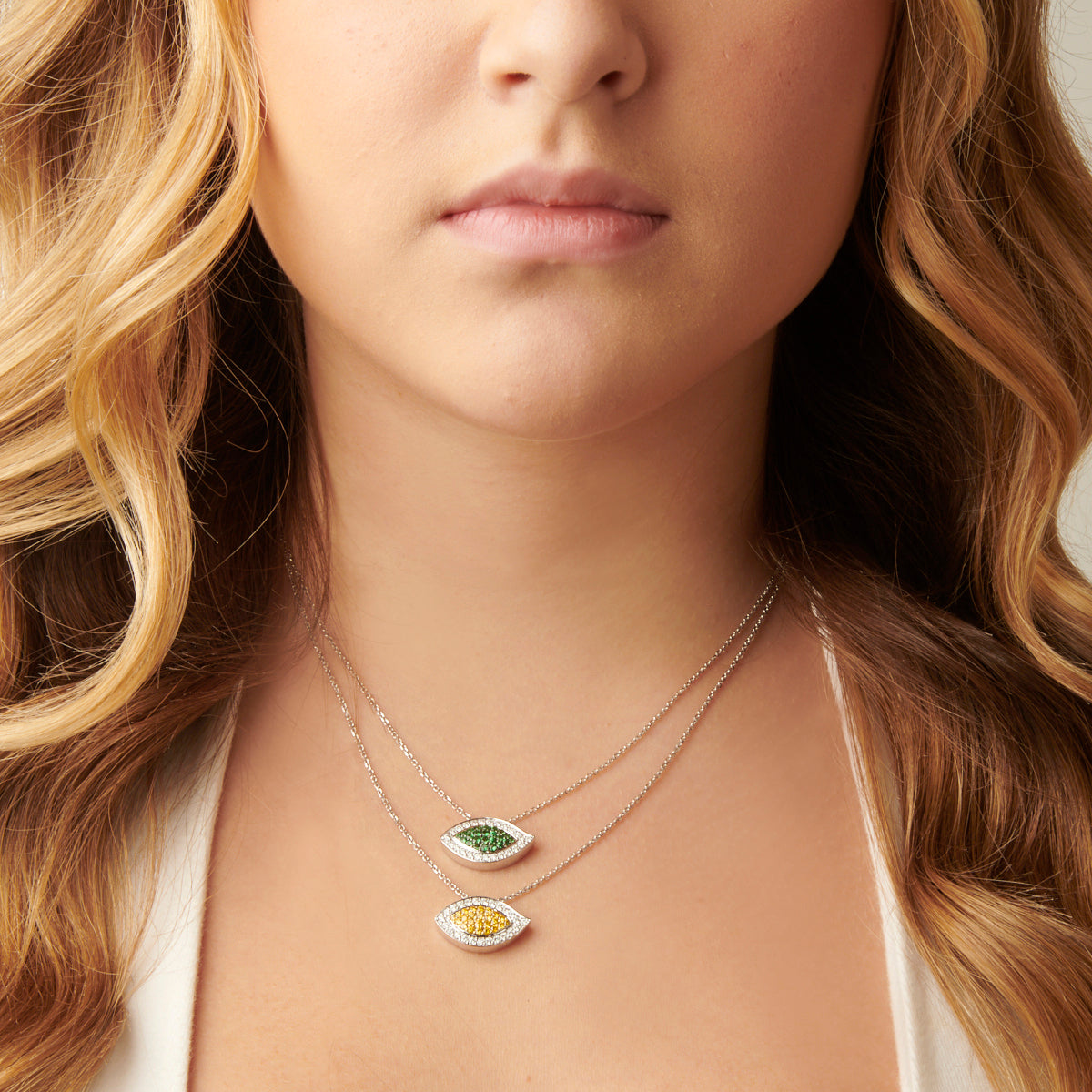 This image shows a woman wearing the Evil Eye Tsavorite and Diamond Pendant. The pendant is hanging from a delicate chain and is centered on the woman's chest. The pendant is a beautiful complement to the woman's outfit and adds a touch of luxury and elegance.