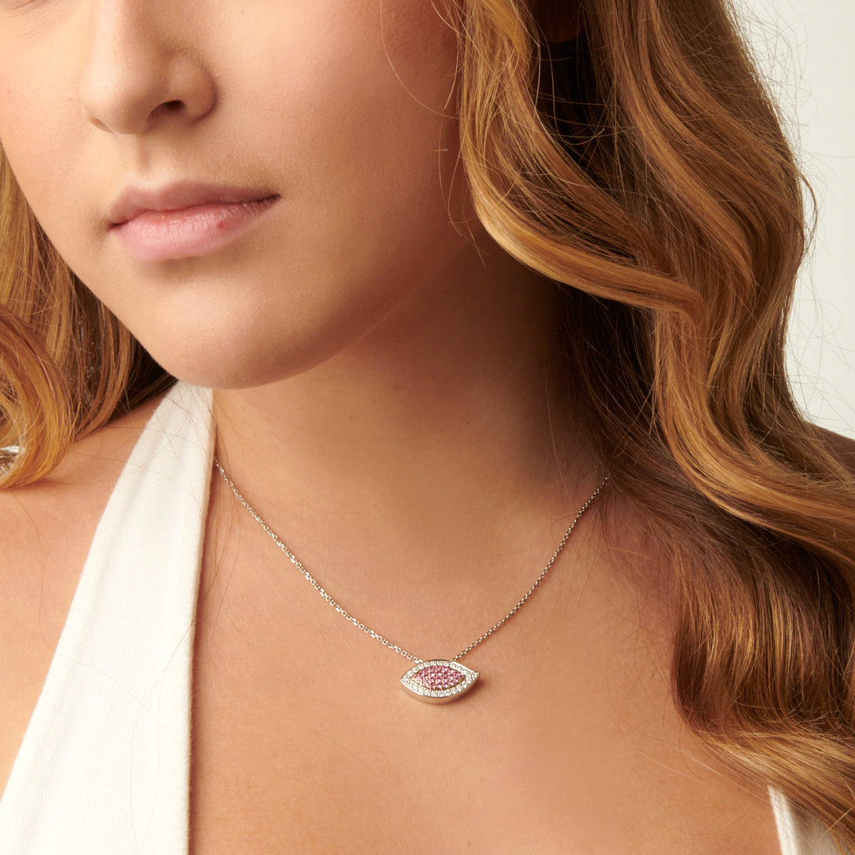A woman wearing an Evil Eye Pink Sapphire and Diamond Pendant. The pendant is suspended from a chain and is resting on the woman's chest.