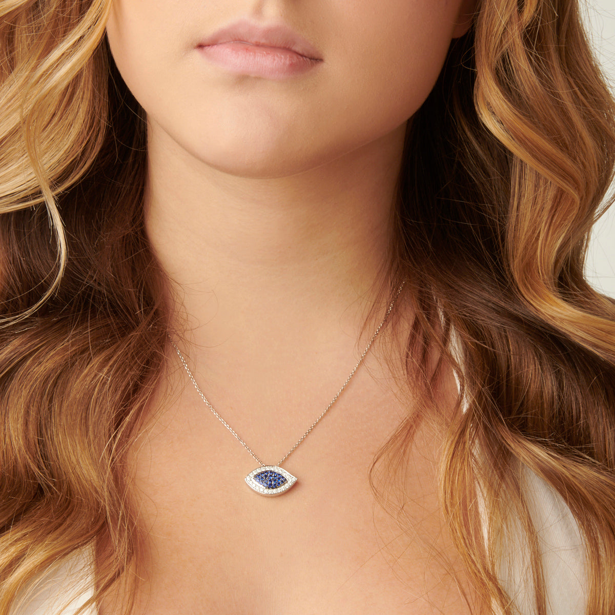 This image shows a woman wearing an Evil Eye Blue Sapphire and Diamond Pendant. The pendant is centered on the woman's neck and is the focus of the image. 