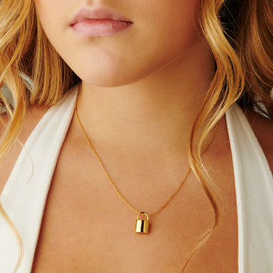 A woman elegantly wearing the Emory Padlock Pendant in 14kt yellow gold, showcasing its charm as it hangs on a delicate chain.