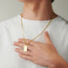 A man wearing the Elon Squadra Pendant Too in 14kt yellow gold. The pendant is hanging from a chain around the man's neck. The man is wearing a whitet-shirt.