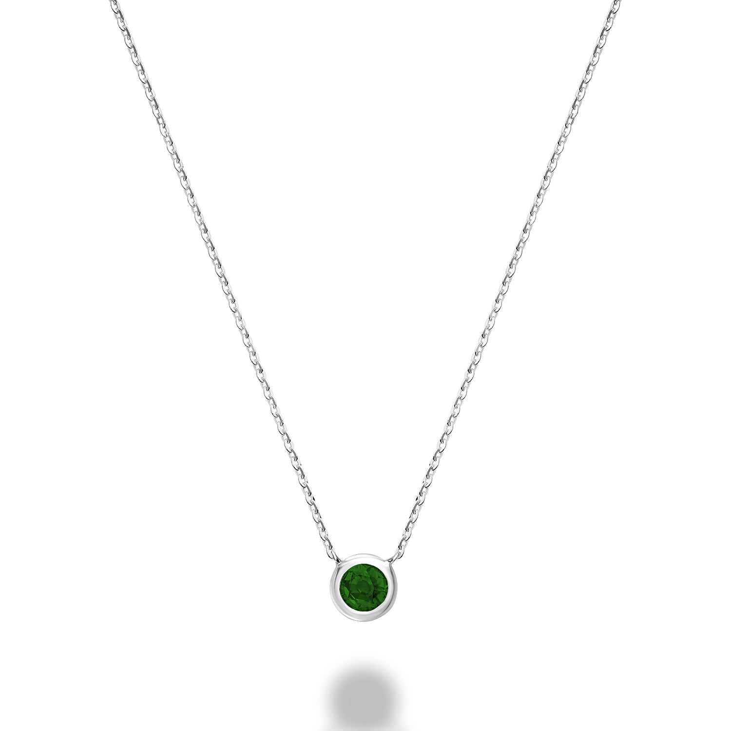 A close-up of a 10kt white gold emerald bezel set necklace. The necklace features a round emerald stone that is set in a gold bezel. The gold is a bright, white color.