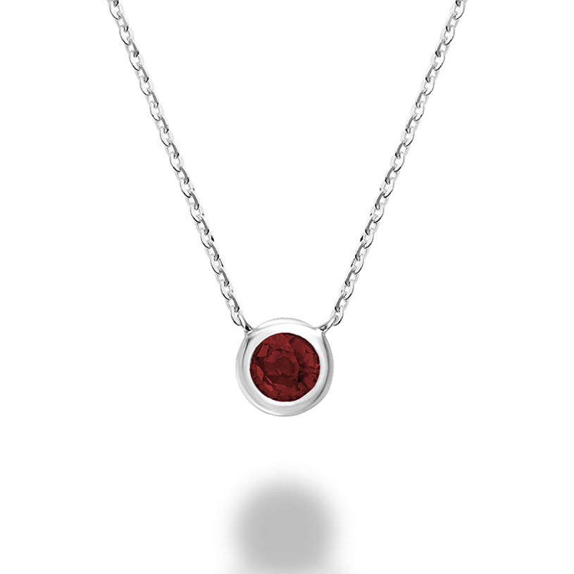 A close-up of a garnet bezel set necklace in 10kt white gold. The necklace features a round garnet gemstone that is set in a bezel setting. The gold is a cool white color.