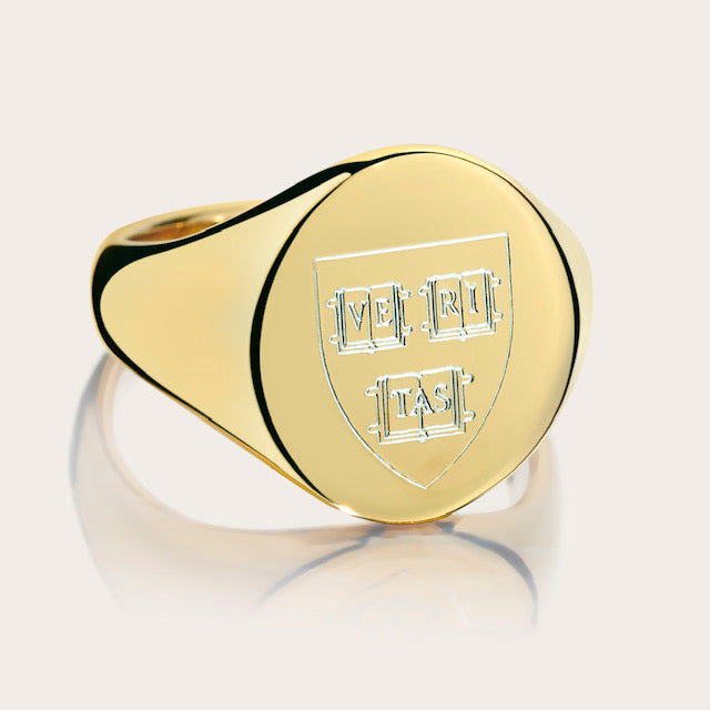 A close-up image of a Harvard Mini Scooped Class Ring made from 14kt solid yellow gold, featuring the Harvard crest on its oval face.