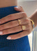 A side view of a woman's hand in focus, adorned with a 14kt solid yellow gold Harvard Mini Scooped Class Ring, showcasing the elegant design and Harvard crest on the ring's oval face.